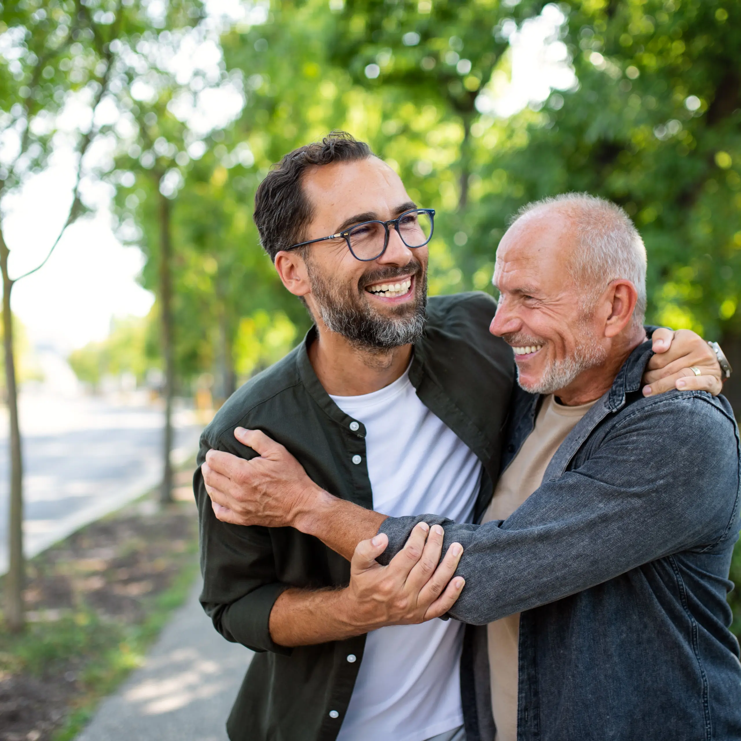 Senior man with his mature son embracing outdoors in park