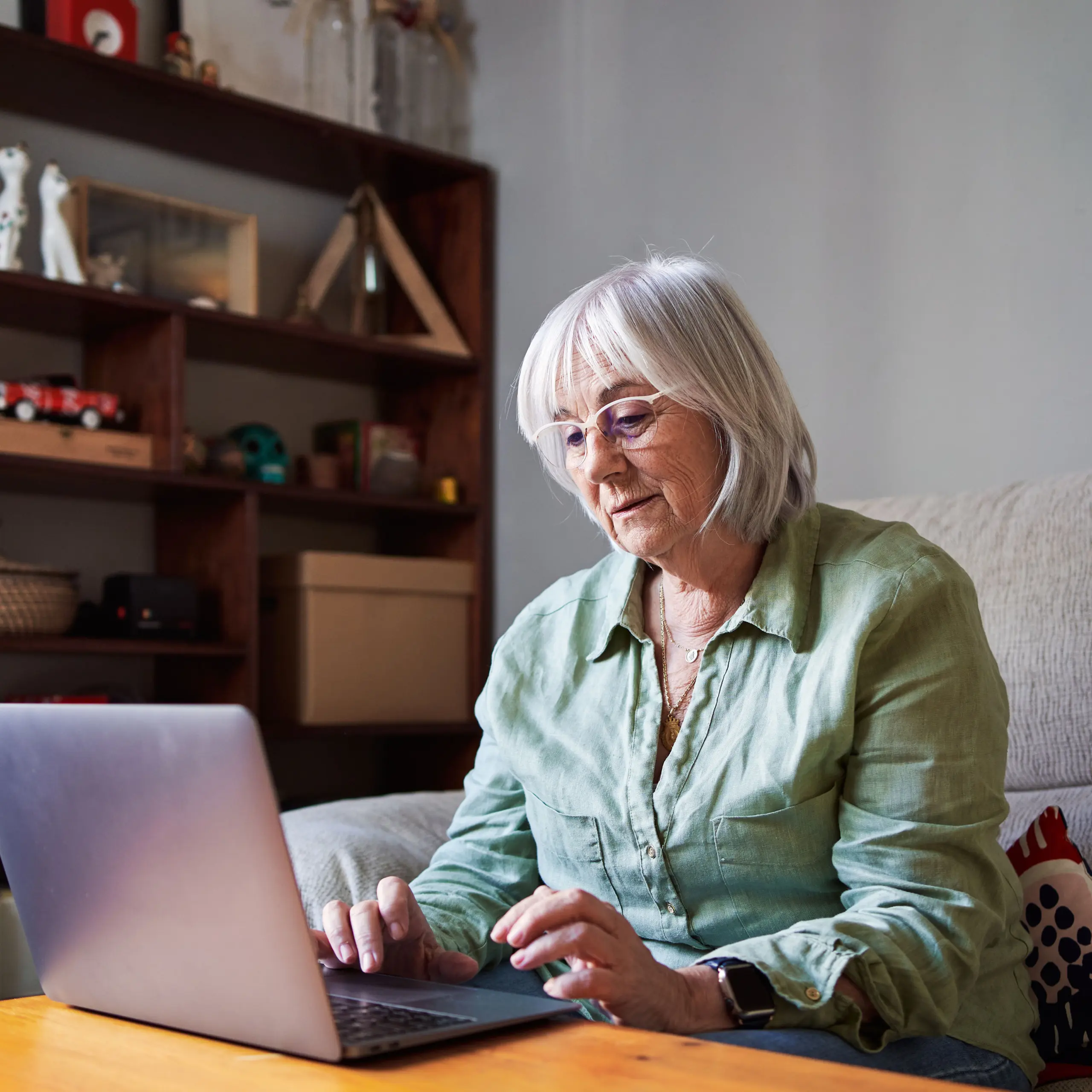 Senior woman using a laptop sitting on the sofa in a house
